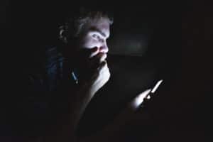 A man looks at his phone in a darkly lit room.